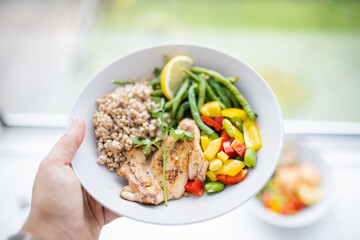 Hand holding a chicken and buckwheat dish with green beans