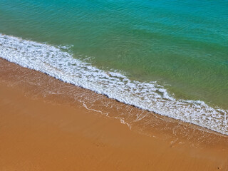 Aerial view of red beach sand with blue ocean and waves