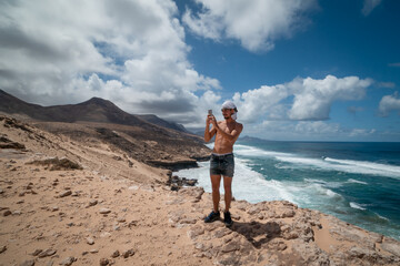 young man stops to take a picture on the edge of the cliff. Jandia. Fuerteventura. Canary Islands