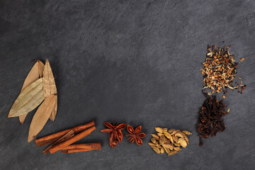 Mix variety spice cinnamon cardamom clove bay leaf wooden border frame copy text space on black slate background