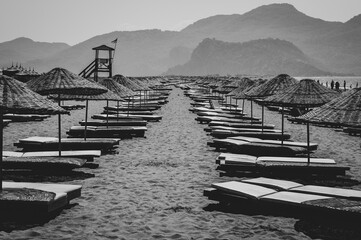 Obraz premium Black-white seascape. Iztuzu Beach near Dalyan town. Long line of sandy beach with sun loungers and parasols. In the bay between the mountains.