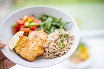 Female hand holding salmon and buckwheat dish with green beans
