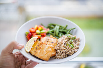 Hand holding salmon and buckwheat dish with green beans