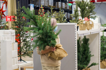 Young woman with protective mask holding a Christmas tree in a shop. Christmas preparations, tradition of buying the Christmas tree. Christmas shopping during the coronavirus pandemic restrictions