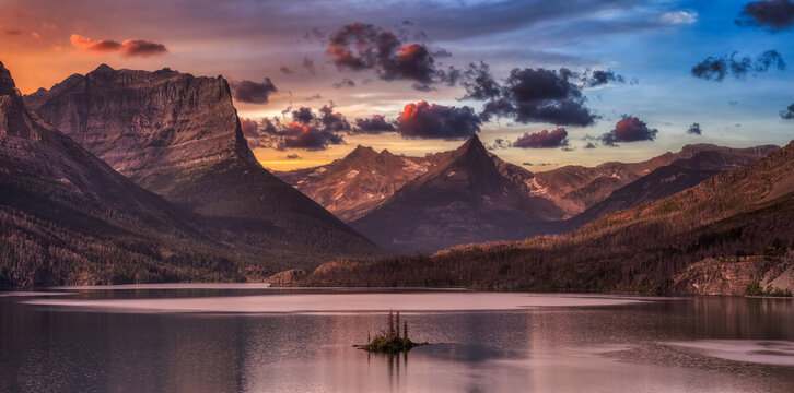 Beautiful Panoramic View of a Glacier Lake with American Rocky Mountain Landscape in the background. Dramatic Colorful Sunrise Sky. Taken in Glacier National Park, Montana, United States.