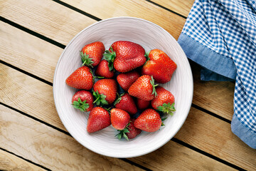 Delicious juicy strawberries on the plate with wooden background.