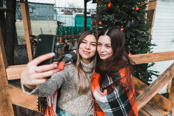 Two cheerful caucasian women friends having fun and making selfie on the backyard with Christmas decorations.