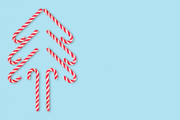 Funny Christmas tree made of candy cane on a blue background. Creative modern minimal composition. Concept of celebration Christmas and New year. Flat lay, top view, copy space