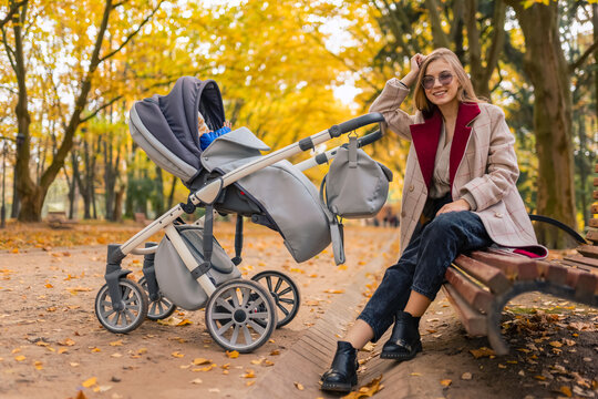 Mother with stroller while walking in the park sat down on bench to rest