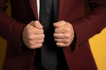 Close up on hands holding a business man burgundy jacket with two hands fixing it on a body isolated on yellow background. 