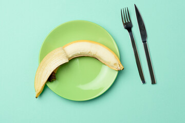 round green ceramic plate with a whole banana and  knife and fork on a green background