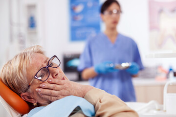 Elderly patient in pain at dentist clinic waiting diagnosis from doctor in medical office. Senior...
