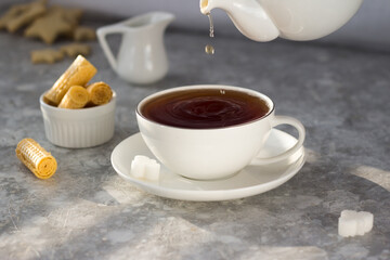 Tea from the teapot is poured into a white mug. A stream of tea pours into the Cup with a splash