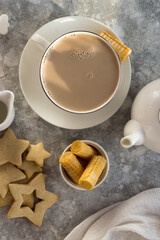 A white mug of tea with milk is on the table. Next to it is waffles, sugar, and a milk jug