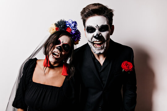 Guy and girl in veil frighteningly pose in images of zombies. Closeup portrait of couple in Mexican style masks