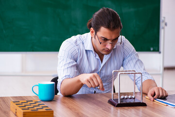 Young male teacher physicist in front of blackboard