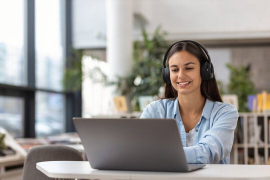 Young Woman Talk On Video Call At The Table Using Headphones. Remote Work Or Learning Concept