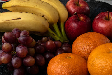 grapes tangerine bananas and apples on a dark pot