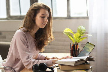 Young teen girl wear headphones at the table, using headphones when studying. Remote learning concept