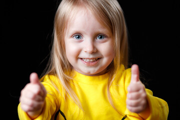 Portrait of a little girl showing thumbs up on a dark background