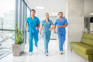 Fototapeta premium Three doctors running throtugh the hospital corridor being in a hurry