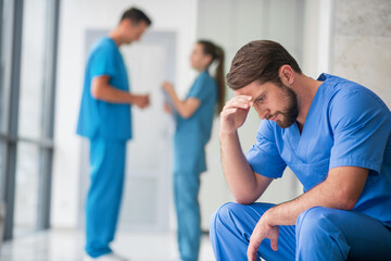 Young male doctor feeling frustrated while his colleagues talking