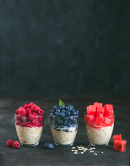Obraz na płótnie Canvas Healthy breakfast:overnight oats with fresh fruits and berries in glass. Overnight oatmeal porridge with watermelon, raspberry,blueberry.Overnight oats on black background,copy space for text.Vertical