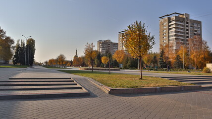 Volzhsky, Volgograd region / Russia - November 5, 2020 Golden autumn trees against the background of the city's central alley with skyscrapers in the background and a temple