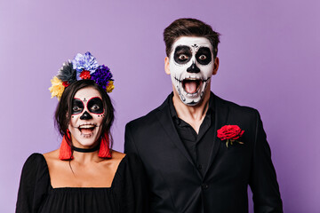 Joyful naughty men and woman in black clothes with red details scream in amazement, posing with Halloween makeup for portrait