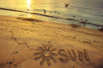 The word SUN written on the beach sand at sunset
