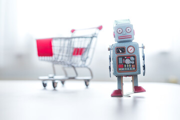 Online shopping algorithm concept. Toy robot on the desk, shopping cart in the blurry background