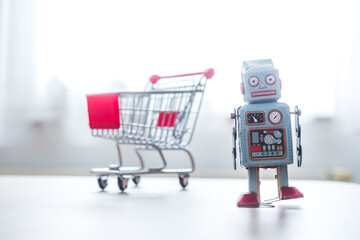 Online shopping algorithm concept. Toy robot on the desk, shopping cart in the blurry background