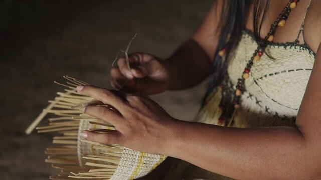 Middle aged woman from the uitoto tribe of the indigenous colombian amazon weaving a typical colombian basket in the foreground