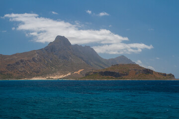  blue clear sea and waves on the surface and rocks and mountains during the day is blue sky in the sky clouds in greece