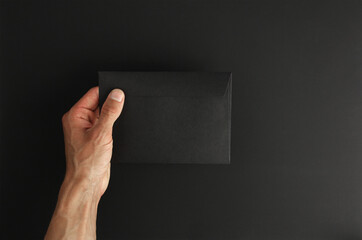 white male hand hold blank black envelope on black background, mockup, copy space