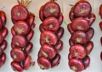 Dangling red onions bunches of heads, harvesting of vegetables, autumn harvest. Bundles of purple onions hanging in the market.Onion storage in russian style.Countryside and autumn harvest in