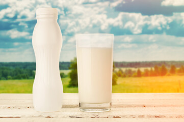 Glass and bottle of milk on wooden table against blur meadow and sky background