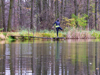 Fototapeta na wymiar Athlete in black green jacket stretching on lake mole or pier outside. Trail runner
