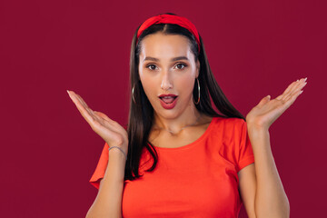 Surprised young female model with long hair, wearing a red shirt, looking at the camera in horror, noticing something unexpected, hearing bad news.