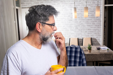 Photo of Sick mature man holding pill and glass of water at home. Serious man ready to take a pill