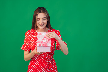 A portrait of a funny, surprised, curious girl in a dress who looks into a gift box, unfolds the gift and looks inside with interest, opening her mouth in amazement.