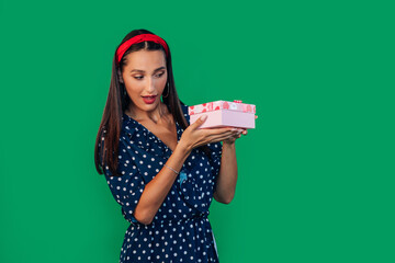 A cheerful woman in a dress holds a gift box and opens it to loo