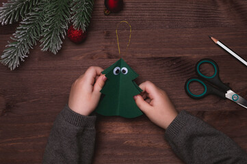 Children crafts. Child makes funny christmas tree toy from paper. Glue toy eyes. Step 3. Top view,...