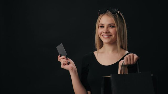 Stylish young woman holding credit card in one hands and shopping bags in another. Happy blonde enjoying black friday period and sales.