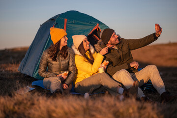 A group of friends camping and taking selfie in front of a tent. 