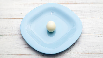 Only one boiled egg on a blue plate on a white wooden background.