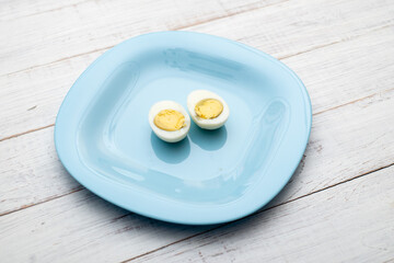 Boiled egg cut into two halves on a blue plate on a white wooden background.