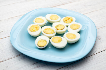 Boiled eggs cut into two halves on a blue plate on a white wooden background.