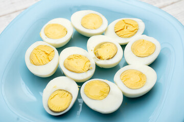 Boiled eggs cut into two halves on a blue plate on a white wooden background.
