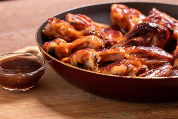 Baked chicken wings with sauce cooked in a pan on a wooden background. Side view. Fast food.